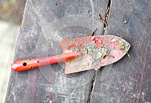 Garden red spade shovel close up photo with soil on the wooden bench