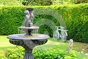 Garden with small fountain and stone bench green lawn plants trees