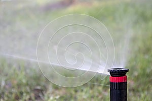 Garden sprinkler in action, spraying water against a soft-focus green background in close-up shot