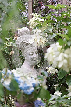 Garden statue. A beautiful stone statue of a woman with a turban and flowers on her hair in the mysteriously secret garden