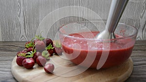 Garden strawberries. Whipped strawberry fruit smoothie with an electric blender. Fresh ripe strawberries in a glass dish, next to