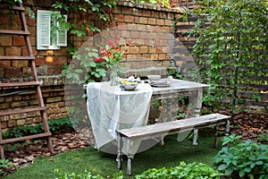 Garden in summer with patio, wooden garden furniture and utensils. Cozy space in patio or balcony. Terrace outdoor with brick wall