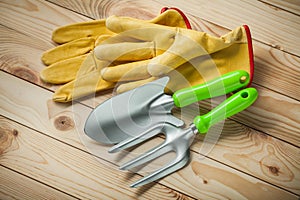 Garden tools. hand spade and fork with yellow leather gloves on wooden background