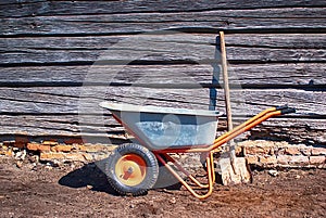 Garden tools stand on the ground next to an old wooden shed on a Sunny day. metal garden wheelbarrow with a shovel, selective focu