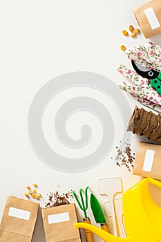Garden tools on a white background. Frame of peat pots, paper bags filled with seeds, a watering can, gloves, and garden shears