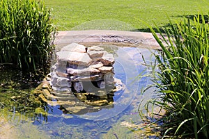 Garden water feature made with natural rocks with lush lawn and tall water grass