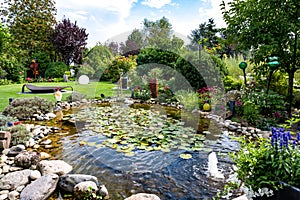 Garden with water lilies on pond, flowerbeds and trees in summer. 