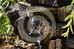 Garden waterfall of stones. Water flows through the stone. The morning sun shines on the waterfall.