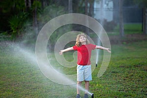 Garden watering systems. Child play with watering sprinkler system in backyard. Little kid playing with garden watering