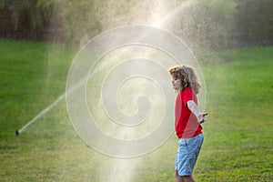 Garden watering systems. Child play with watering sprinkler system in backyard. Little kid playing with garden watering