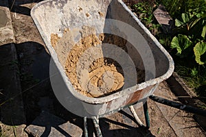 A garden wheelbarrow filled with sand and dry cement mixture stands on the path