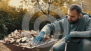 Garden worker who is a man loading dry leaves and tree branches on to a wheelbarrow