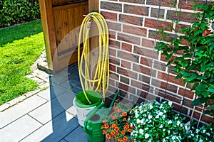 A garden yellow hose connected to a tap protruding from a farm building against a background of brick facade, a photo closeup.