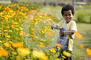 In the garden, a young African boy can be seen joyfully playing with a watering device.