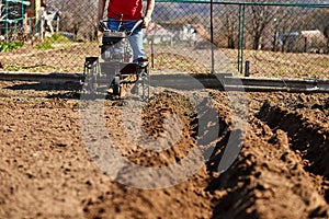 Gardener cultivate ground soil with tiller tractor or rototiller, cutivator