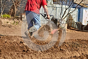 Gardener cultivate ground soil with tiller tractor or rototiller, cutivator