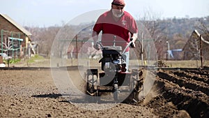 Gardener cultivate ground soil with tiller tractor or rototiller, cutivator