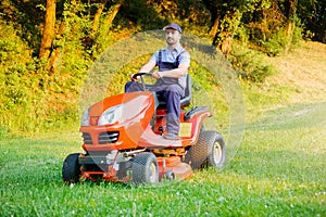 Gardener driving a riding lawn mower in garden