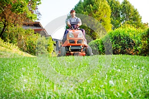 Gardener driving a riding lawn mower in garden