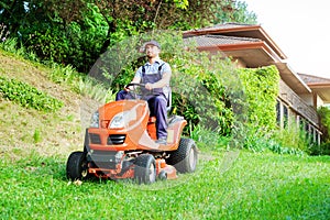 Gardener driving a riding lawn mower in garden