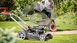 Gardener emptying lawn mower grass into a wheelbarrow after mowing.