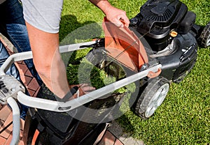 Gardener emptying lawn mower grass into a wheelbarrow after mowing.