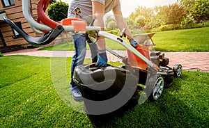 Gardener emptying lawn mower grass into a wheelbarrow after mowing.