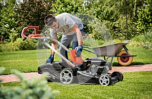 Gardener emptying lawn mower grass into a wheelbarrow after mowing.