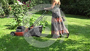Gardener girl in flip-flop shoes mow lawn with grass cutter in yard. 4K