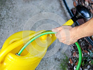 Gardener with a green garden hose is pouring water in yellow watering bucket. Garden yellow water can for watering flowers.