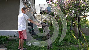 Gardener holding hand hose sprayer and watering plants in garden