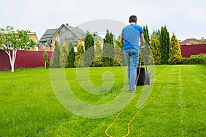 A gardener with a lawn mower is cutting grass in the garden in the house backyard