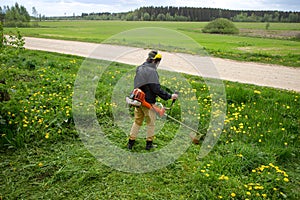 The gardener man mows the grass with yellow dandelions with a hand lawn mower. close up trimmer, selective focus