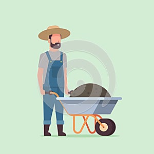 Gardener man pushing wheelbarrow full of earth compost male farmer working in garden wearing overalls gardening concept