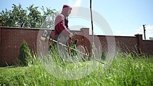 Gardener mows green grass with a gasoline mower, the plants scatter to the sides