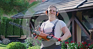 Gardener posing on back yard with electric trimmer in hands