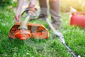 Gardener preparing grass trimmer on lawn in garden outdoors. photo