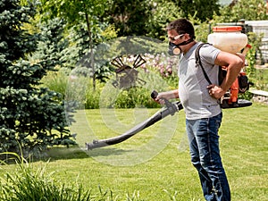 Gardener in protective mask and glasses spraying toxic pesticides trees