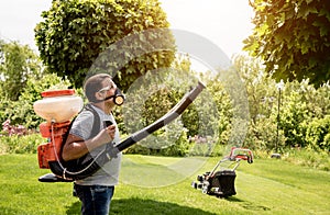 Gardener in protective mask and glasses spraying toxic pesticides trees