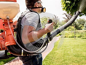 Gardener in protective mask and glasses spraying toxic pesticides trees