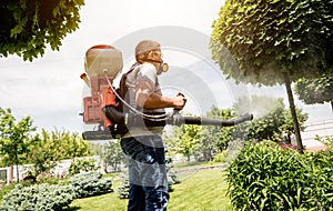 Gardener in protective mask and glasses spraying toxic pesticides trees