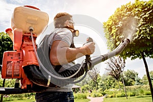 Gardener in protective mask and glasses spraying toxic pesticides trees