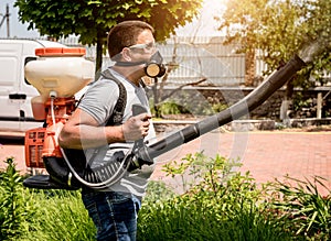 Gardener in protective mask and glasses spraying toxic pesticides trees