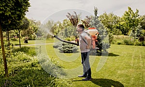 Gardener in protective mask and glasses spraying toxic pesticides trees