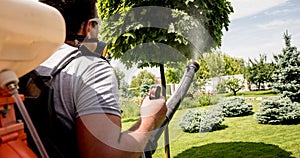 Gardener in protective mask and glasses spraying toxic pesticides trees