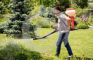 Gardener in protective mask and glasses spraying toxic pesticides trees