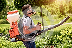 Gardener in protective mask and glasses spraying toxic pesticides trees