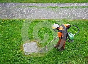 A gardener, with protective mask and work overalls, cuts the grass with a professional trimmer