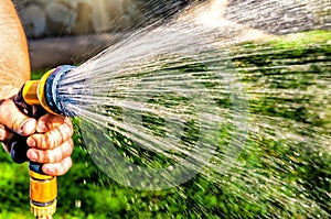 Gardener\'s hand holds a hose with a sprayer and watered green lawn garden