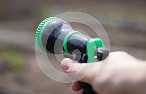 The gardener`s hand holds a hose with a sprayer and waters the plants in the garden. Green atomizer in hand with a large lan.